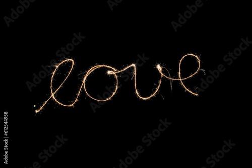 Long exposure shot of the sparking word "love" written and isolated in the black empty background