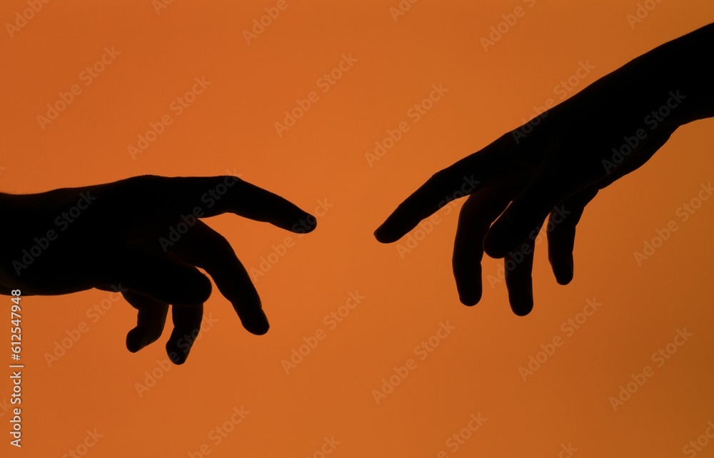 Silhouette shot of two hands reaching for each other, isolated on an orange background