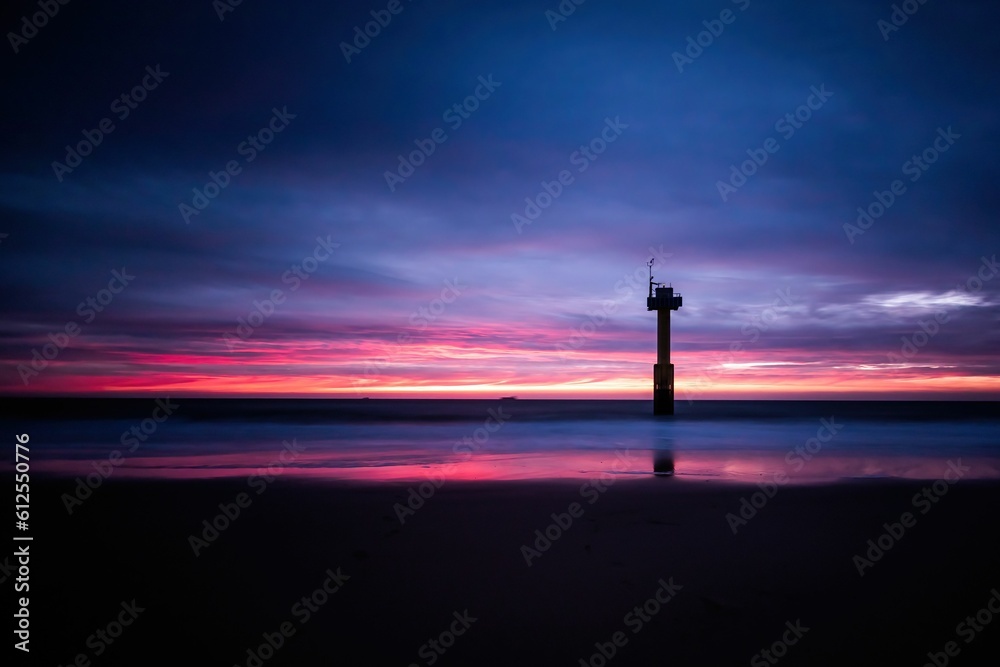 Naklejka premium Distant shot of a distant building and its reflection on the seawater at a vibrant sunset