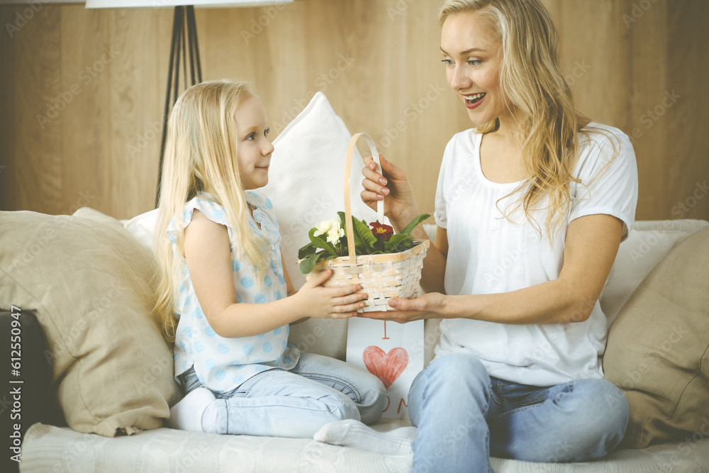 Happy mother day. Child daughter congratulates mom and gives her basket of spring flowers and postcard with heart drawing. Family and childhood concepts.