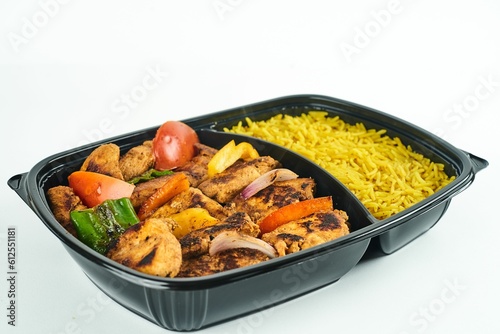 Rice and roasted meat and vegetables in a black container against white background