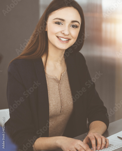 Young business people are talking to each other  while sitting at the desk in sunny office. Businesswoman is explaining something to her colleague.