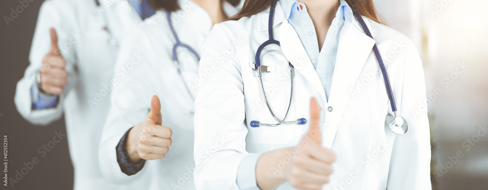 Group of doctors standing as a team with thumbs up in sunny clinic. Good news and Hope for a cure. Medicine concept during Coronavirus pandemic. Covid-2019. Group of doctors standing as a team with thumbs up in sunny clinic. Good news and Hope for a cure. Medicine concept during Coronavirus pandemic. Covid-2019.