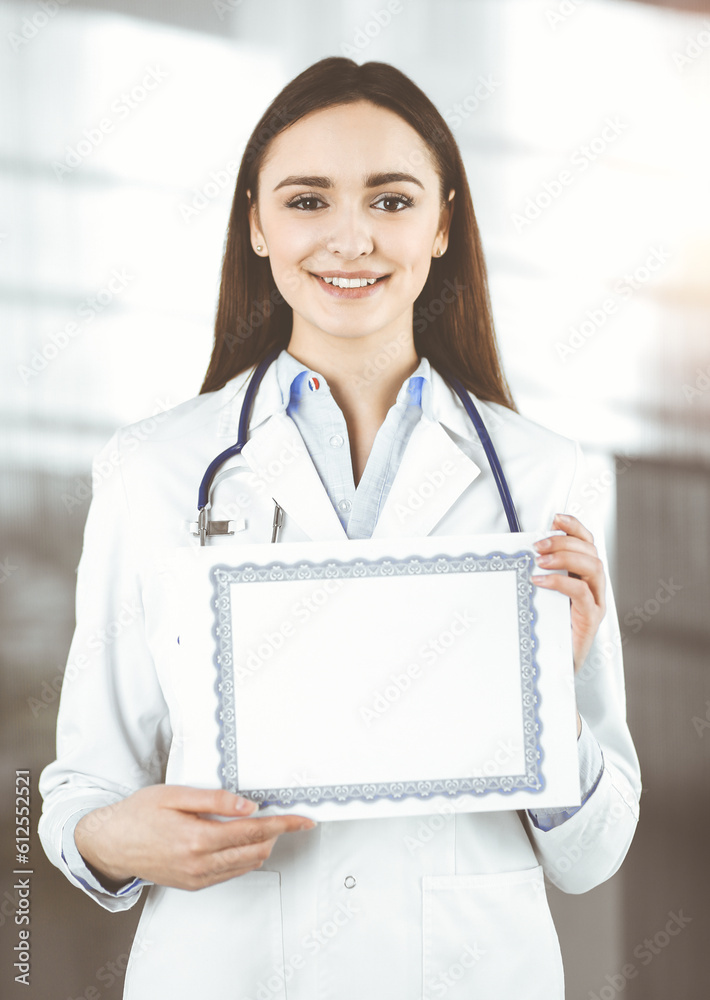 Happy young woman-doctor is holding a certificate in her hands. Professional physician at work in sunny clinic. Happy young woman-doctor is holding a certificate in her hands. Professional physician at work in sunny clinic.