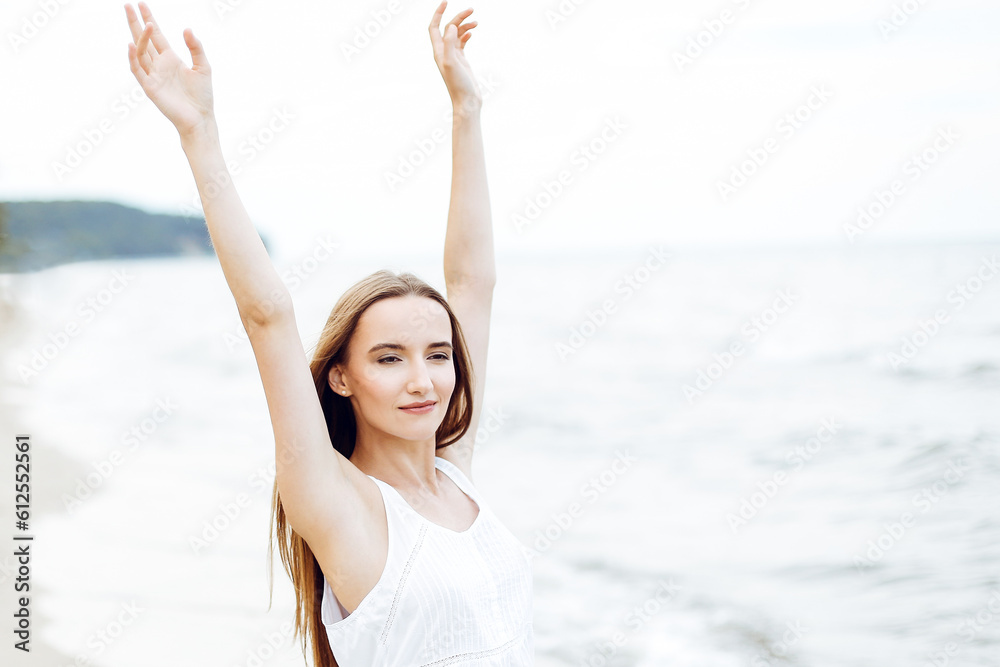 Happy smiling woman in free happiness bliss on ocean beach standing with raising hands. Portrait of a multicultural female model in white summer dress enjoying nature during travel holidays vacation o Happy smiling woman in free happiness bliss on ocean beach standing with raising hands. Portrait of a multicultural female model in white summer dress enjoying nature during travel holidays vacation o