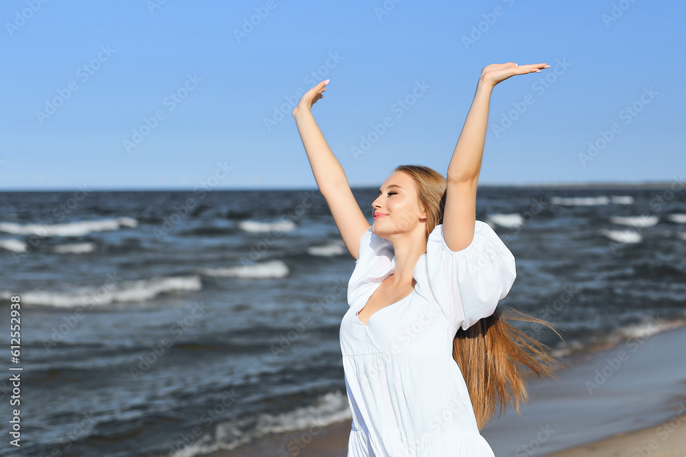 Happy smiling beautiful woman on the ocean beach standing in a white summer dress, raising hands. Happy smiling beautiful woman on the ocean beach standing in a white summer dress, raising hands.