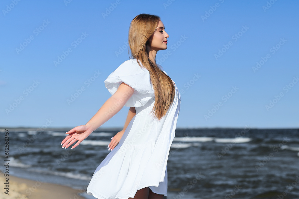 Happy smiling beautiful woman is on the ocean beach in a white summer dress, open arms. Happy smiling beautiful woman is on the ocean beach in a white summer dress, open arms.