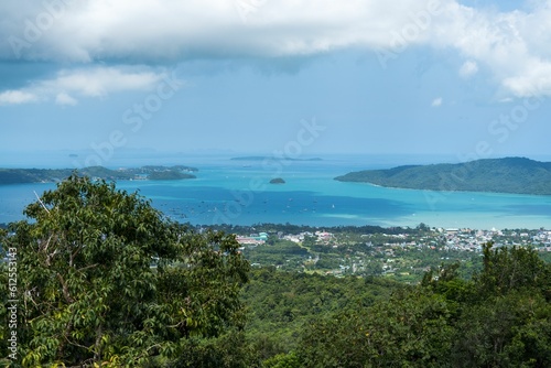 Scenic view of a tranquil sea and a coastal town against a blue sky captured from an evergreen hill