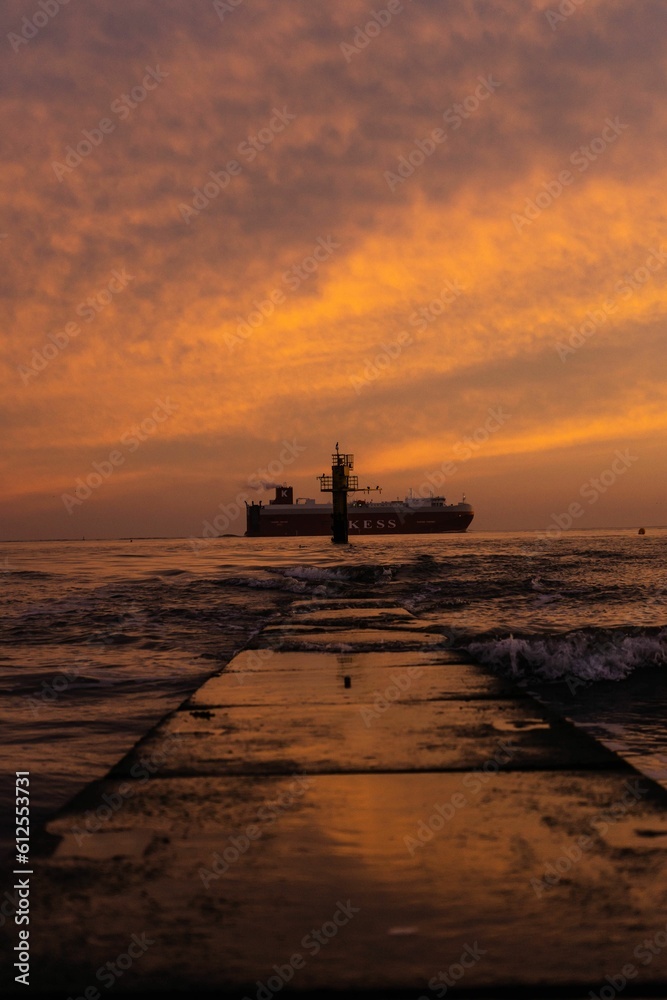 Vertical shot of a dock and a ship in the distance during a golden sunset
