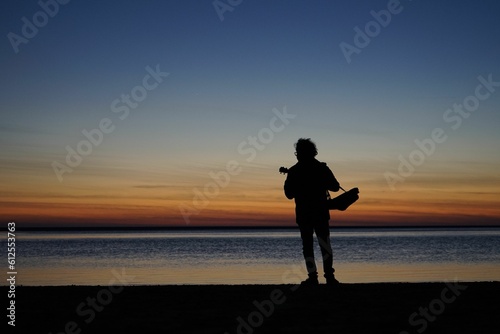Silhouette of male playing thukulele in front of sea during sunset