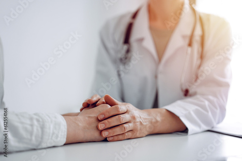 Doctor and patient sitting at the desk in clinic office. The focus is on female physician s hands reassuring woman  close up. Perfect medical service  empathy  and medicine concept.