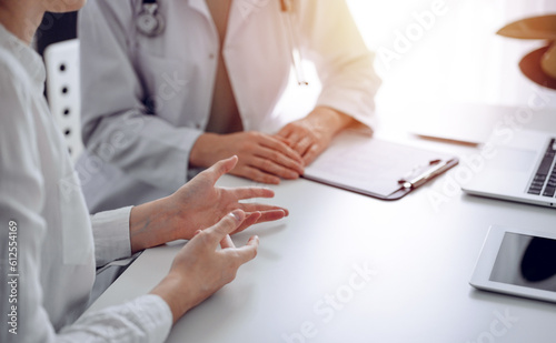 Doctor and patient discussing current health examination while sitting at the desk in clinic office. The focus is on female patient s hands  close up. Perfect medical service and medicine concept.