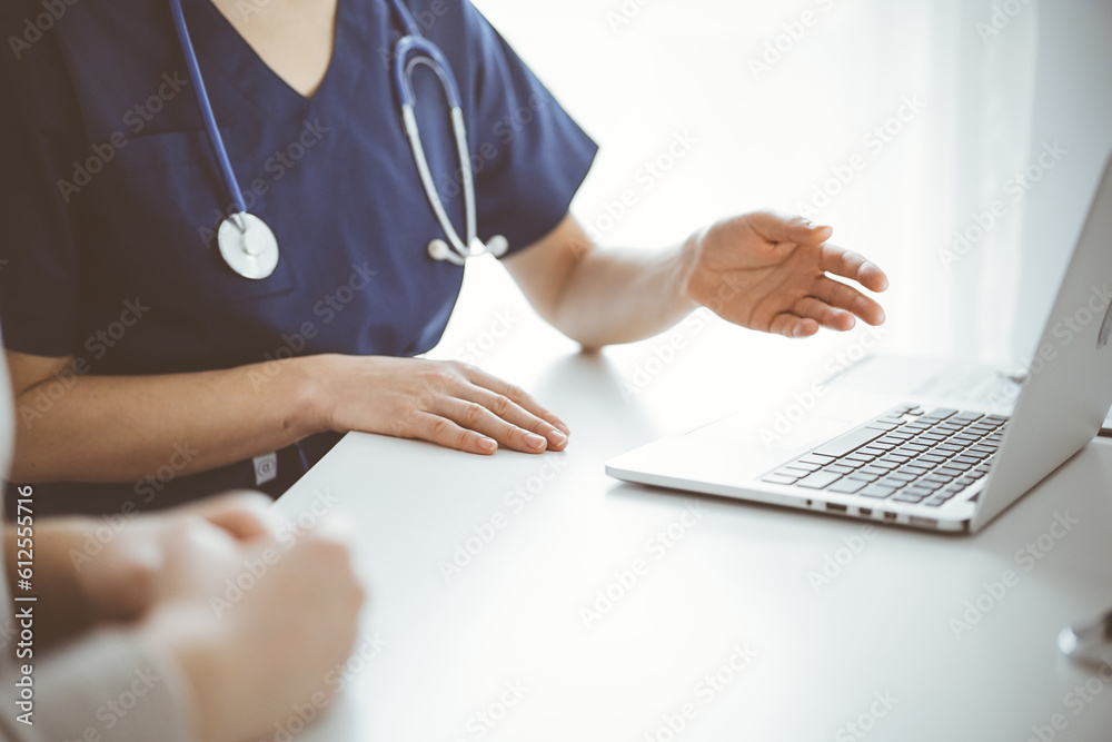 Doctor and patient sitting at the table in clinic. The focus is on unknown female physician's hand pointing to laptop computer monitor, close up. Medicine concept. Doctor and patient sitting at the table in clinic. The focus is on unknown female physician's hand pointing to laptop computer monitor, close up. Medicine concept.