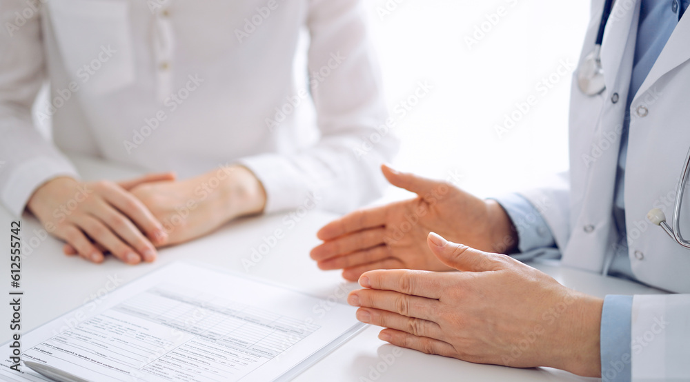 Doctor and patient discussing current health questions while sitting near of each other and using clipboard at the table in clinic, just hands closeup. Medicine concept.