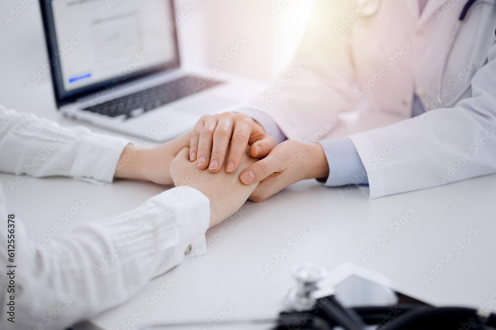 Doctor and patient sitting opposite each other at the table in clinic office. The focus is on female physician's hands reassuring woman, only hands, close up. Medicine concept. Doctor and patient sitting opposite each other at the table in clinic office. The focus is on female physician's hands reassuring woman, only hands, close up. Medicine concept.