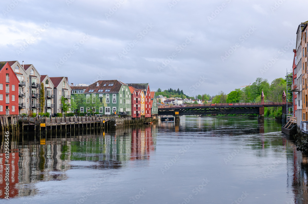 A row of typical colourful Norwegian houses built on pillars on top of a water surface. Reflecting on the water surface.