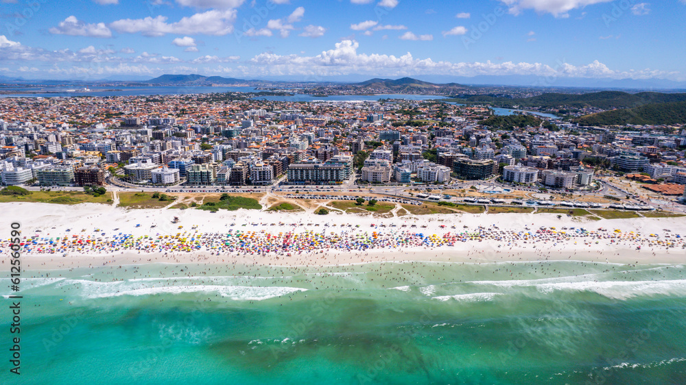 Drone view on the beach with sea and waves and white sand, tourists with umbrella