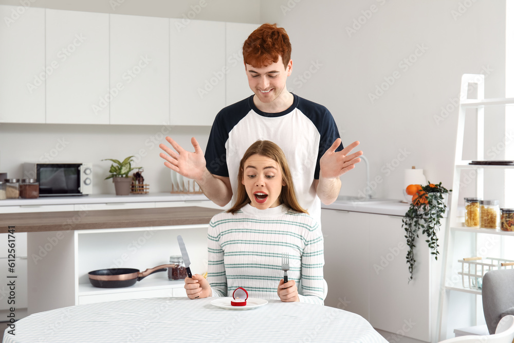 Young man proposing to his happy girlfriend in kitchen Young man proposing to his happy girlfriend in kitchen