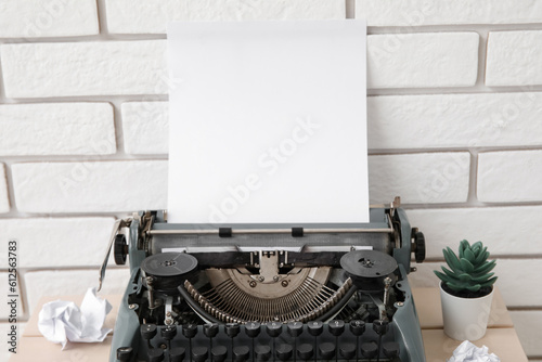 Vintage typewriter with crumpled paper and houseplant on table near brick wall