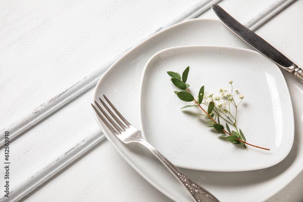 Plates with silver cutlery and flowers on white wooden background Plates with silver cutlery and flowers on white wooden background