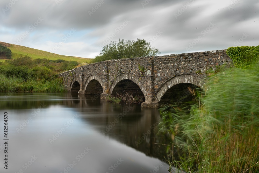 Long exposure of a wide river water with a stone bridge stretching from one side of it to the other