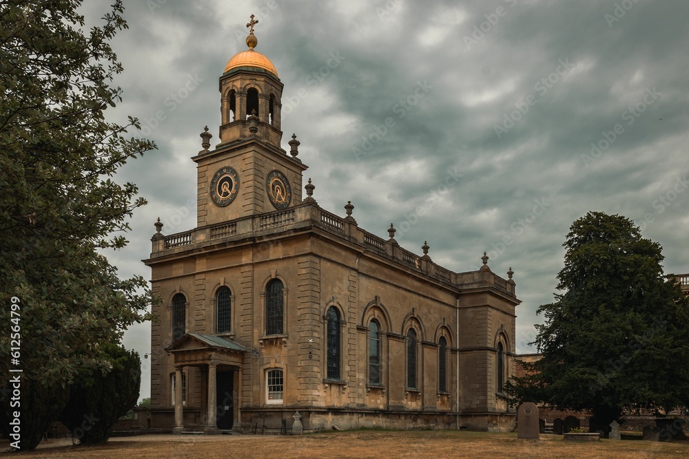 Horizontal shot of the Witley Court building surrounded by green trees and under the cloudy sky