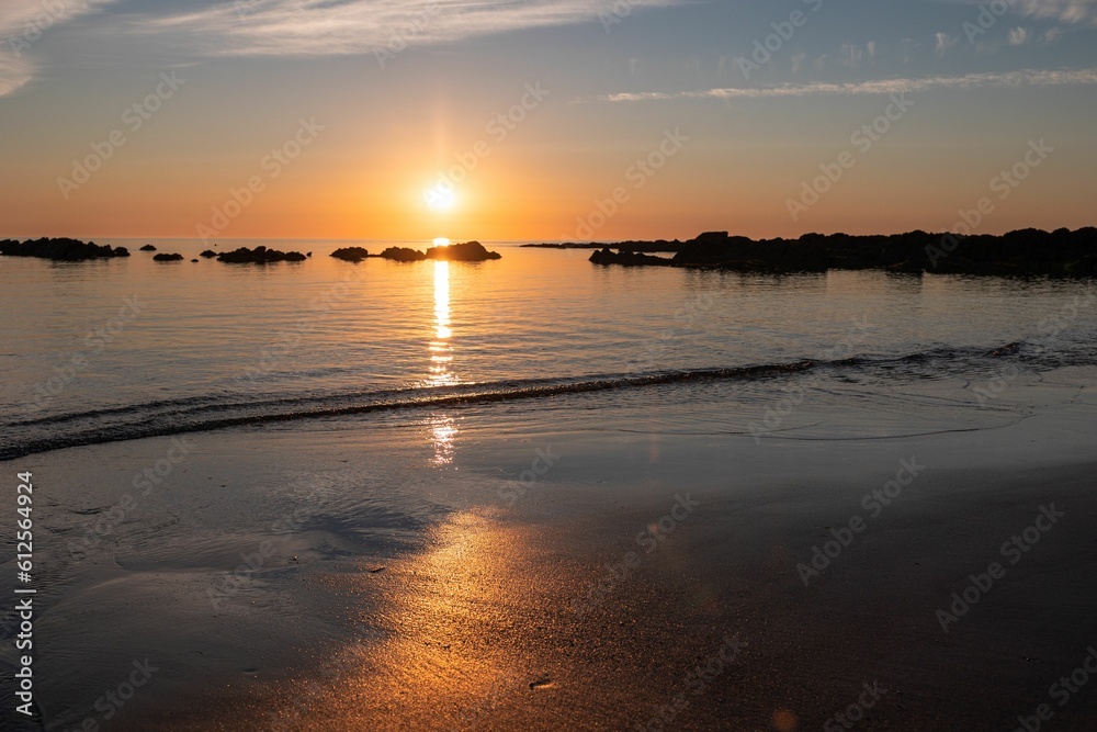 Bright sun in colorful sunset sky shining above the sea seen from wet sandy beach