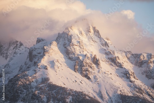 Snowy peaks of the Grand Tetons mountains hiding behind the clouds on a sunny day