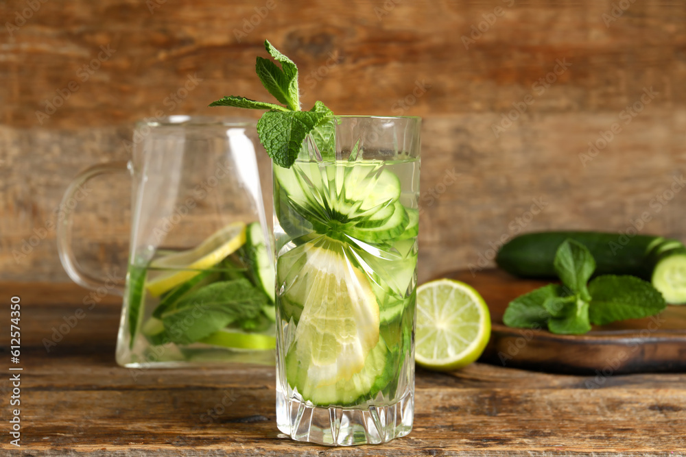 Glass and jug of infused water with cucumber slices on wooden background Glass and jug of infused water with cucumber slices on wooden background