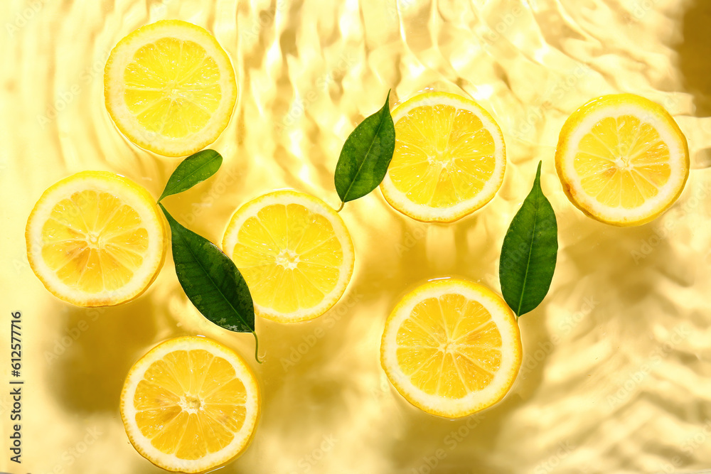 Slices of fresh lemon and leaves in water on yellow background Slices of fresh lemon and leaves in water on yellow background