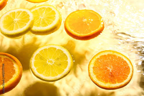 Slices of fresh orange and lemon in water on yellow background