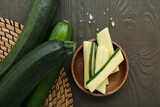 Fresh green zucchini and bowl with slices on black wooden background