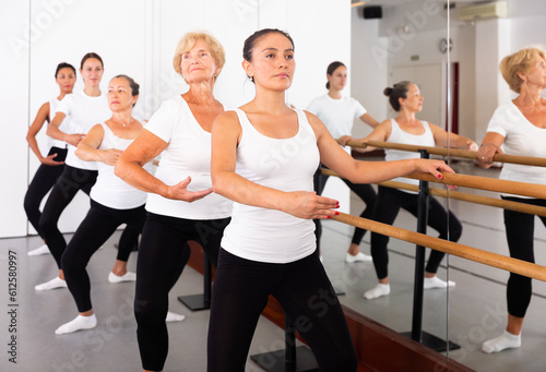 Women of different ages exercising ballet moves in training room.