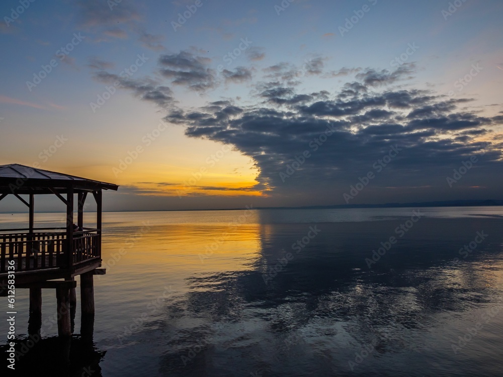 Wooden pier at the shore with a beautiful calm sunset in the horizon