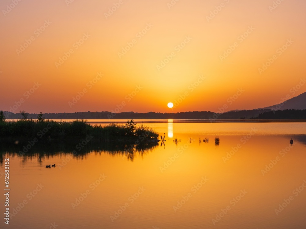 Peaceful scenery of the horizon and a lake with silhouettes during the sunset with orange sky