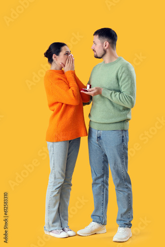 Young man proposing to his girlfriend on yellow background © Pixel-Shot