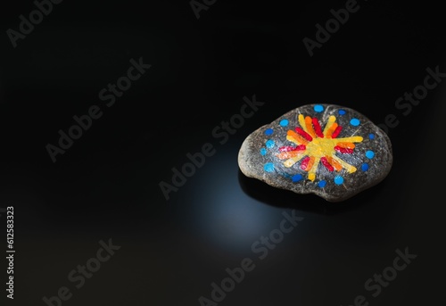 Stone with colorful painting on a dark background with space for text