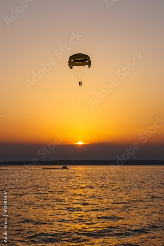 Vertical shot of two people paragliding and enjoying the beautiful sunset visible on the horizon