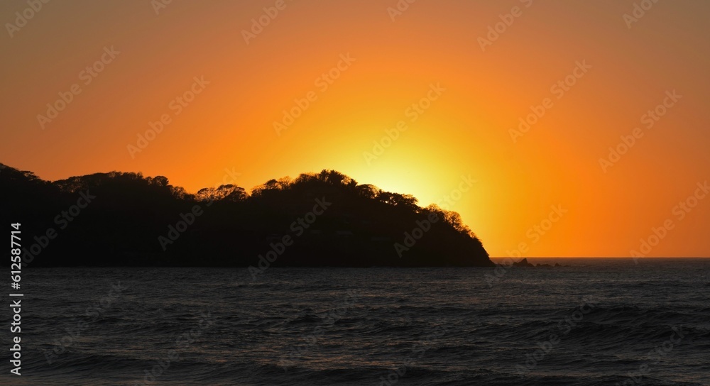 Silhouette of an island against the glowing sun in the sunset sky