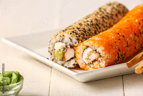 Plate with tasty sushi rolls on white wooden background, closeup