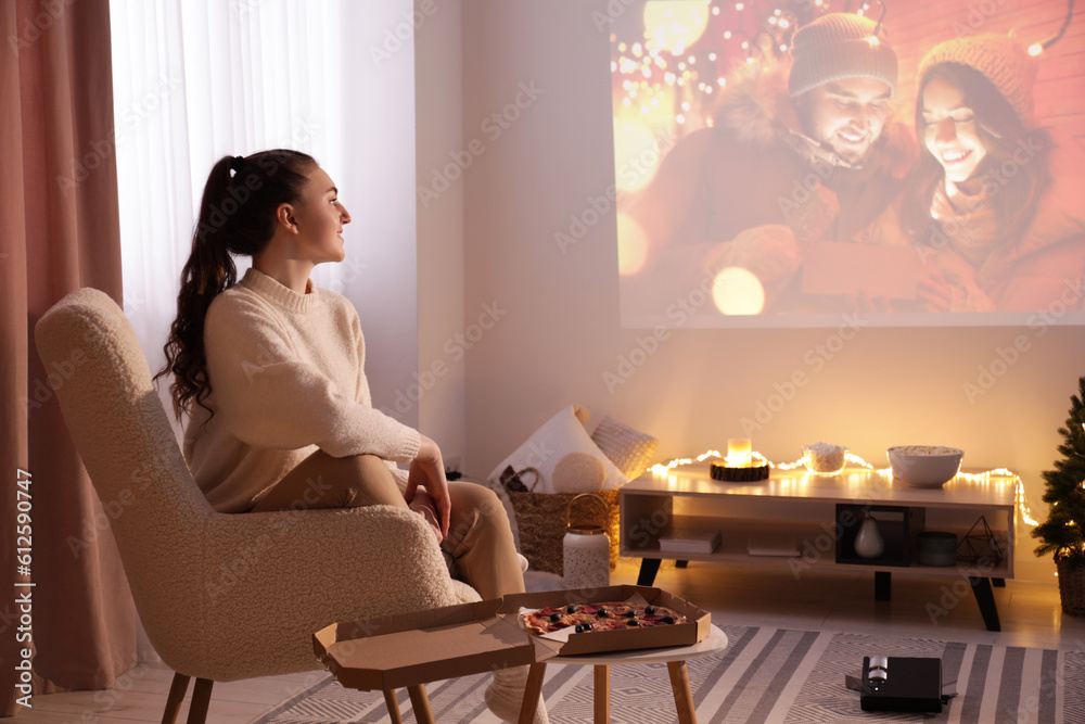 Woman watching romantic Christmas movie via video projector at home - obrazy, fototapety, plakaty 