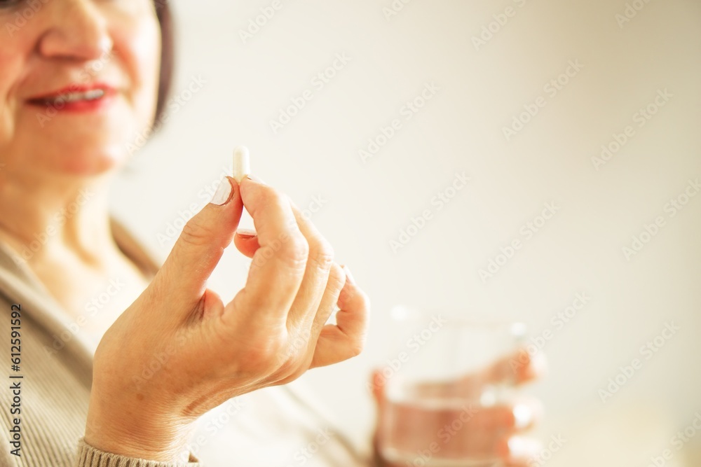 Fototapeta premium Close up of a retired woman in casual clothes at home holding pill and glass water. 