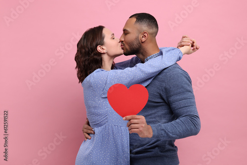 Lovely couple with red paper heart kissing on pink background. Valentine's day celebration