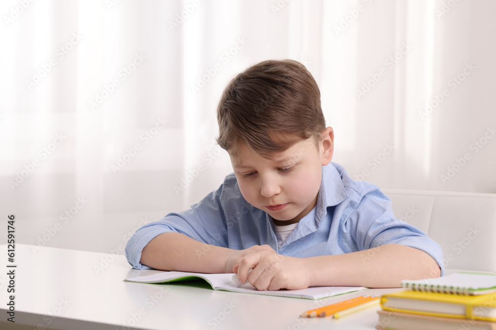 Little boy erasing mistake in his notebook at white desk indoors Little boy erasing mistake in his notebook at white desk indoors