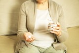 Middle aged unrecognized woman sitting at home, holding glas of fresh water and taking medicine.