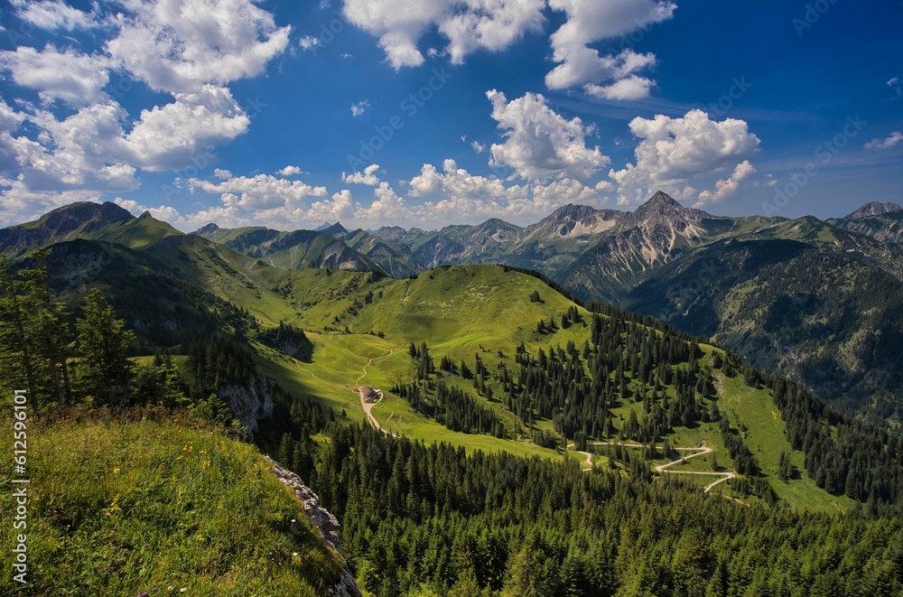 Bird's eye view of a mountain range covered with green forests under a cloudy blue sky