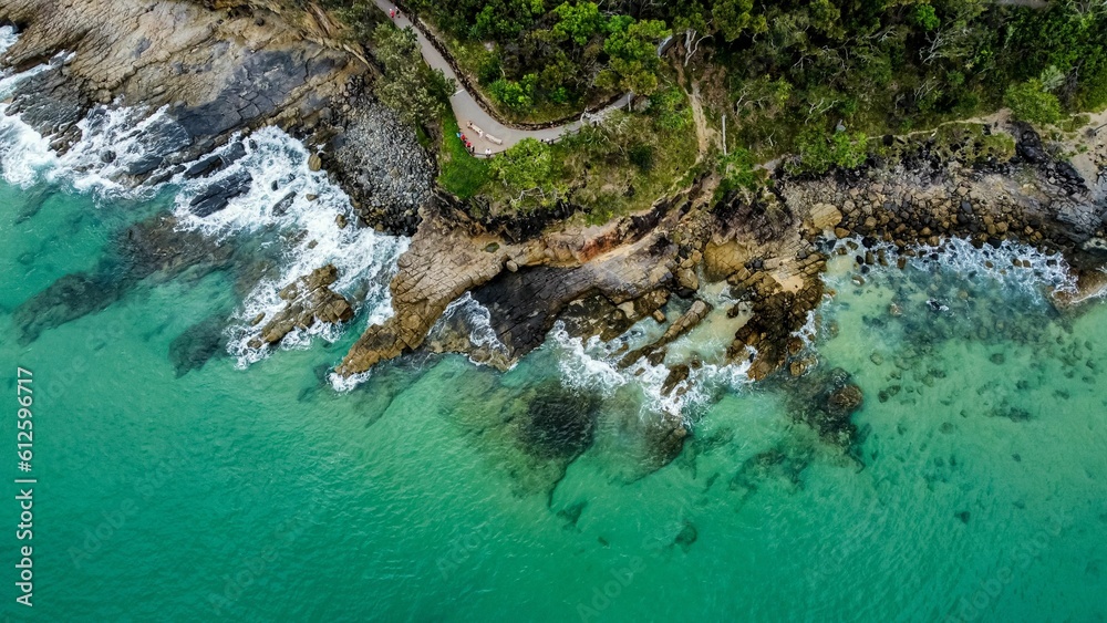 Aerial view of the turquoise ocean waves hitting the rocky coast on a sunny day Aerial view of the turquoise ocean waves hitting the rocky coast on a sunny day
