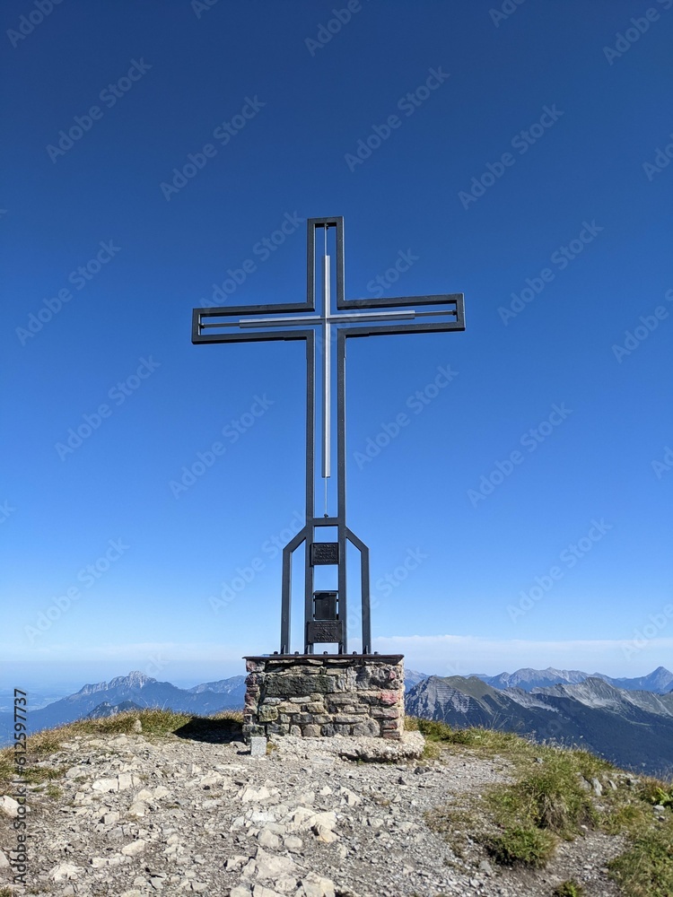 Beautiful vertical view of a cross statue on a rocky mountain against blue sky