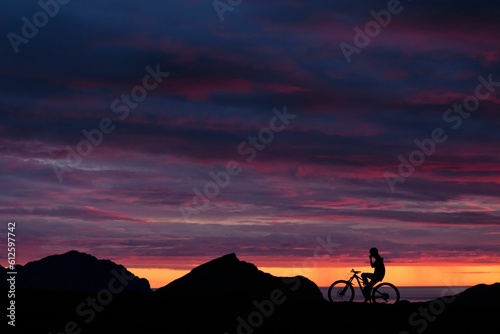 Beautiful sunset sky over the silhouettes of a cyclist and hills.