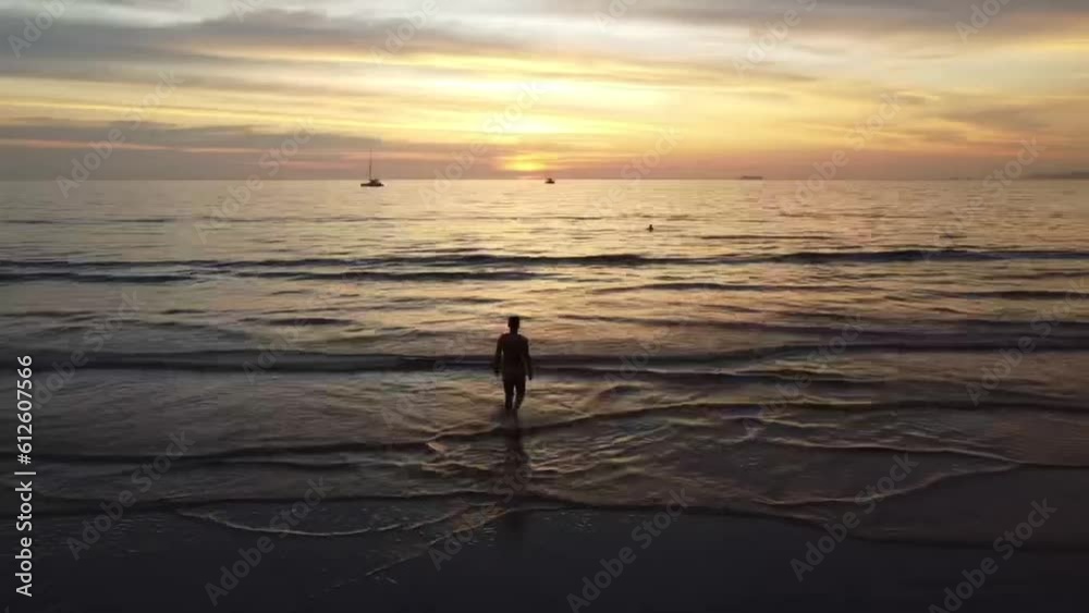 Drone view of the beautiful seascape with a person approaching waves at sunset Drone view of the beautiful seascape with a person approaching waves at sunset
